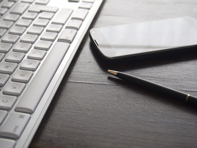 Keyboard, smartphone and pen on a dark desk