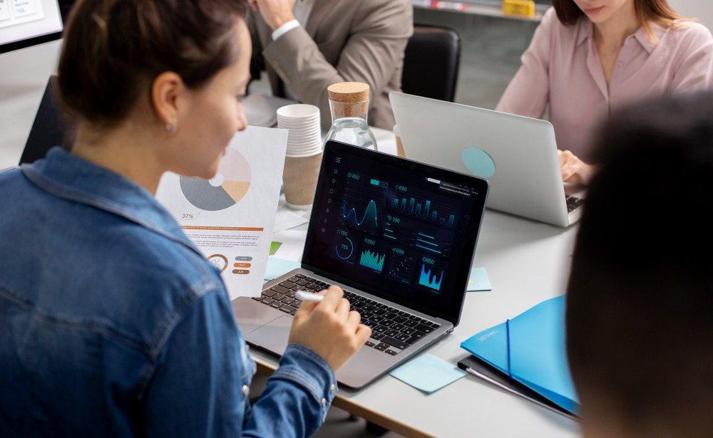 Colleagues around a table looking at a laptop that shows charts, next to a printed report