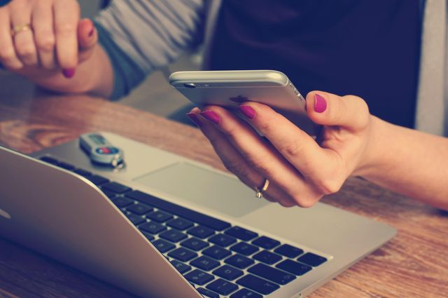 Person using a smartphone next to a laptop